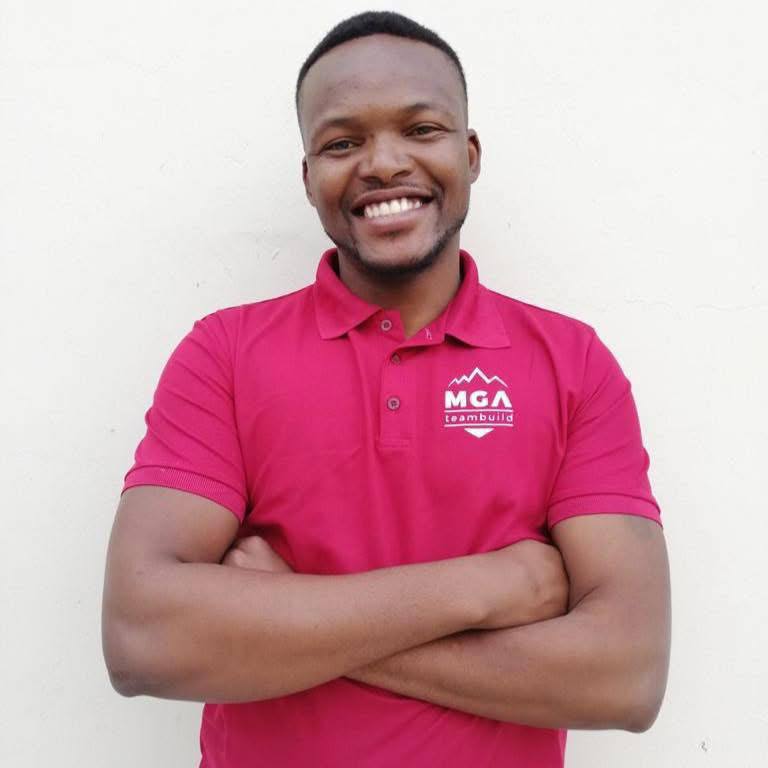 Sakhumzi Klaas, founder of MGA-Teambuild, smiling with arms crossed in an MGA-branded shirt
