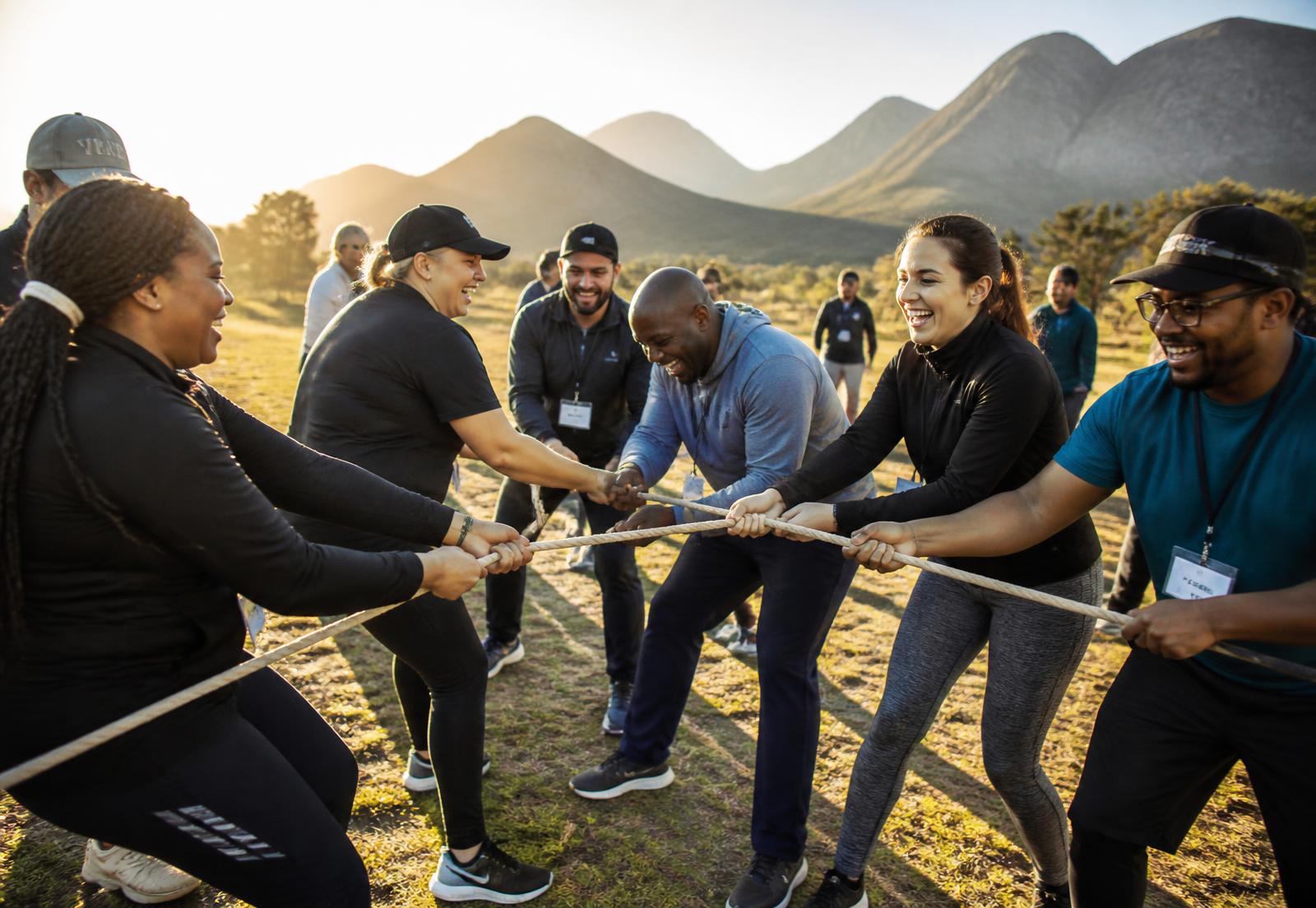 Diverse South African team laughing during an outdoor tug-of-war team-building activity with mountains behind them